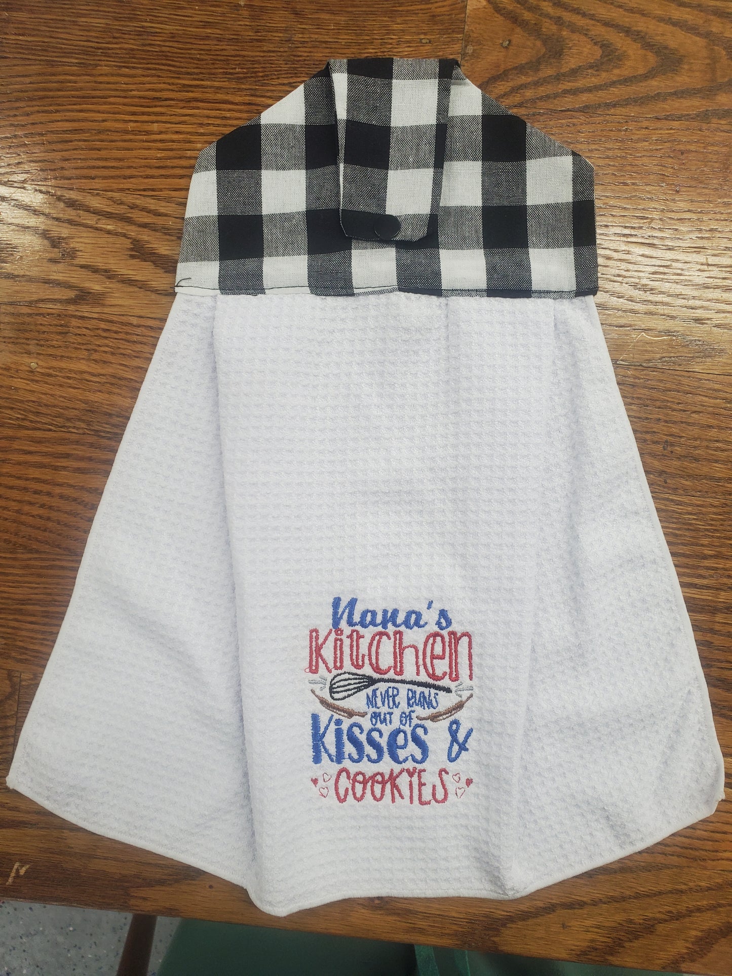 White kitchen towel with plaid border and embroidered text Nana's  Kitchen never runs out of kisses and cookies