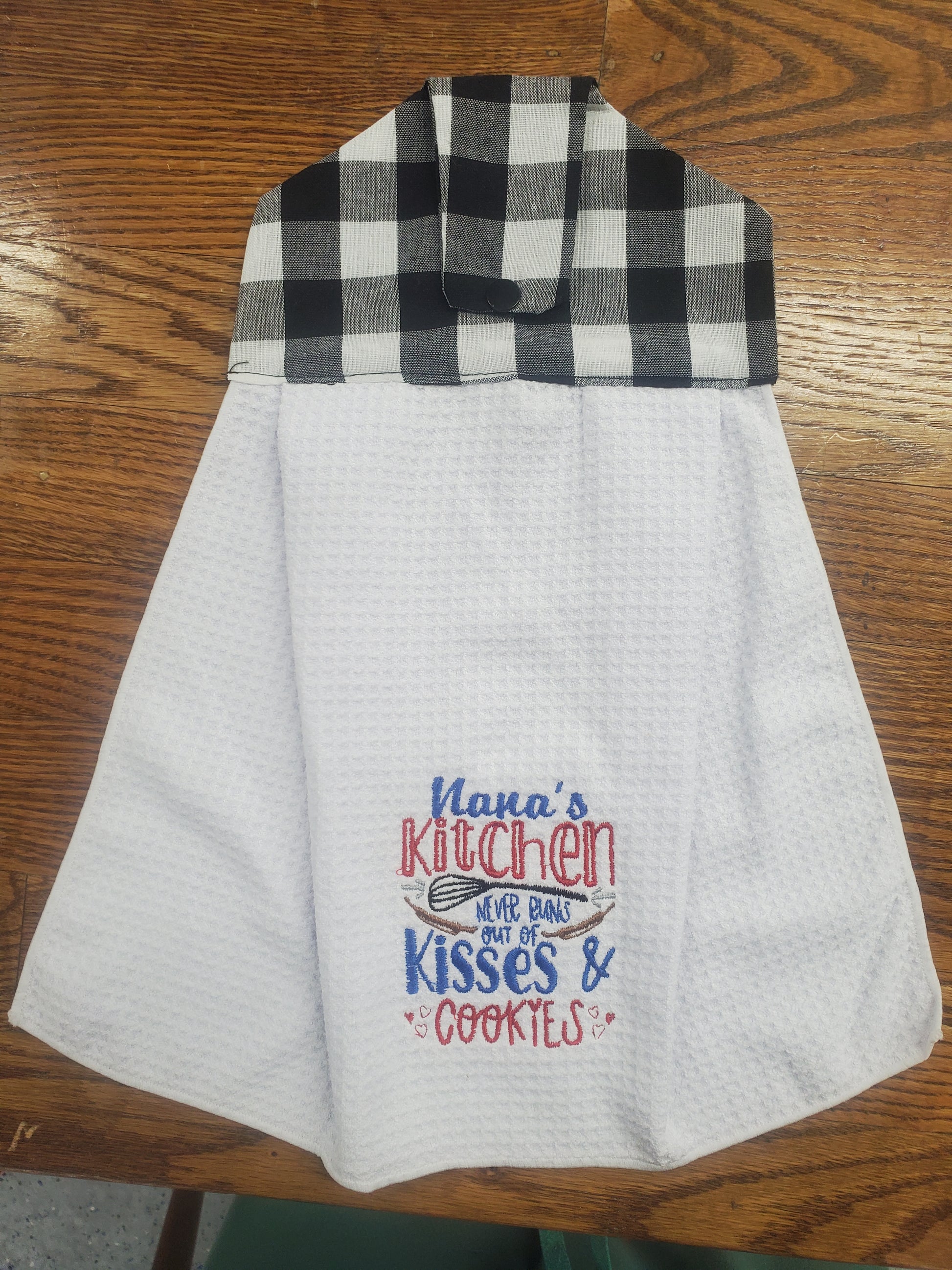 White kitchen towel with plaid border and embroidered text Nana's  Kitchen never runs out of kisses and cookies