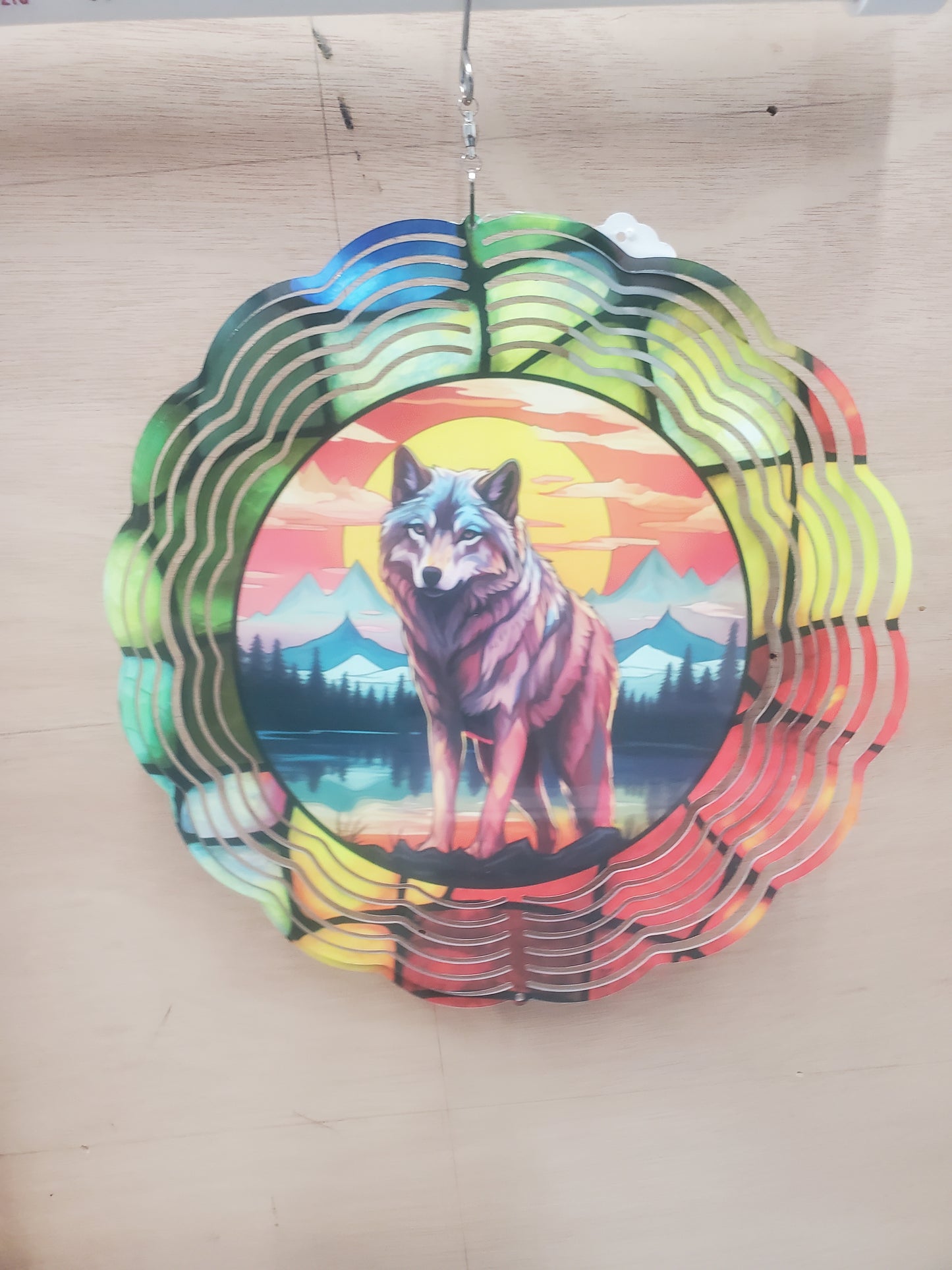 A circular wind spinner with a colorful sunset and wolf design in the center.